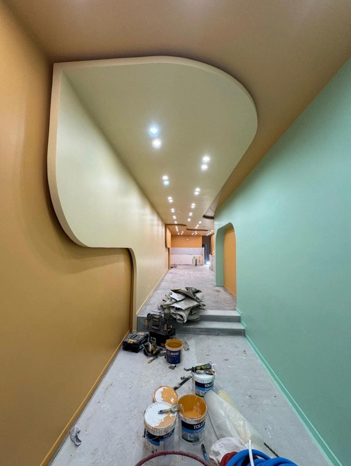 Gang met gebogen gyprocplafond, inbouwspots en kleurrijk schilderwerk